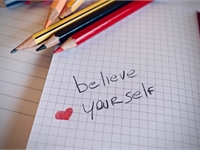 pens an a notebook with believe yourself written